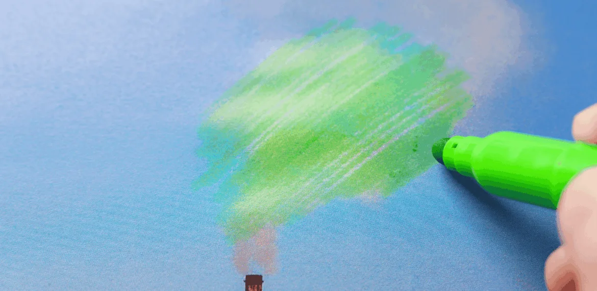 A hand uses a green marker to draw over smoke coming from a factory chimney, making it look like tree foliage against a blue sky.