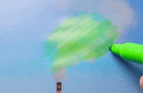 A hand uses a green marker to draw over smoke coming from a factory chimney, making it look like tree foliage against a blue sky.